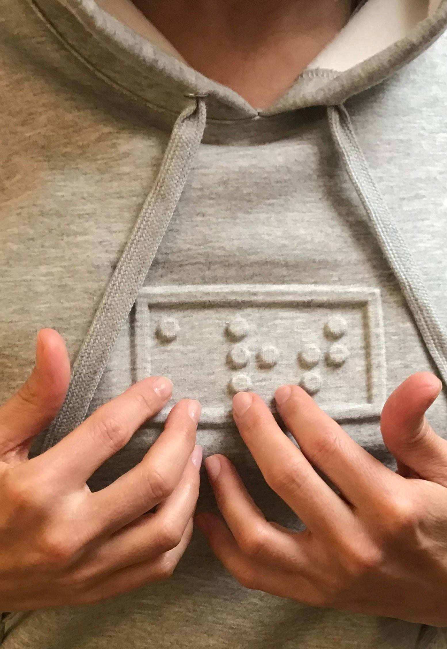 gros plan d'un hoodie gris avec 'art' embossé en braille sur la poitrine.